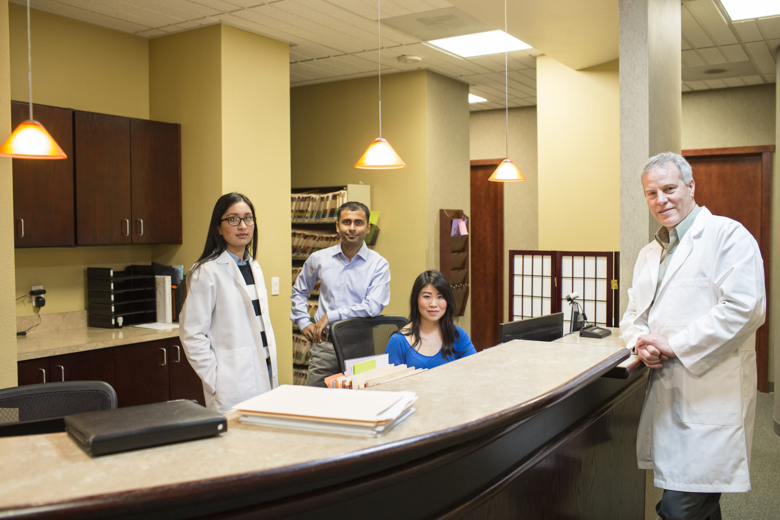 Caucasian male and east Indian woman ophthalmologists in their office with their staff employees.